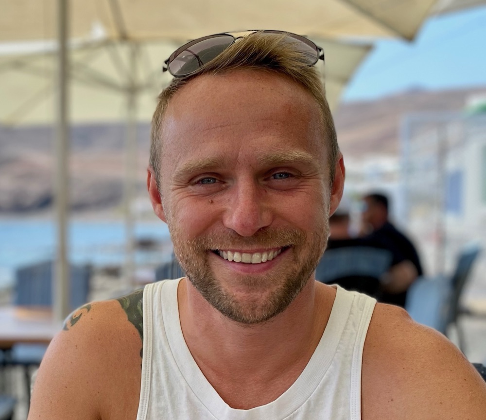 Kamil wearing Energetic Health and EMF Protection Amulets, seated on the beach gazing at the sea, embodying calm and balance